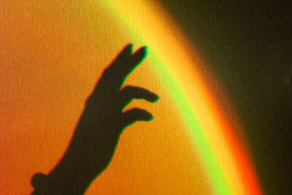 Shadow of womans hand. Rainbow reflection of sunbeam on wall. Hand touches rainbow.